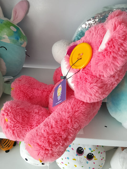 Fairgame brand pink teddy bear plush toy with a yellow button eye and a stitched "X" eye.