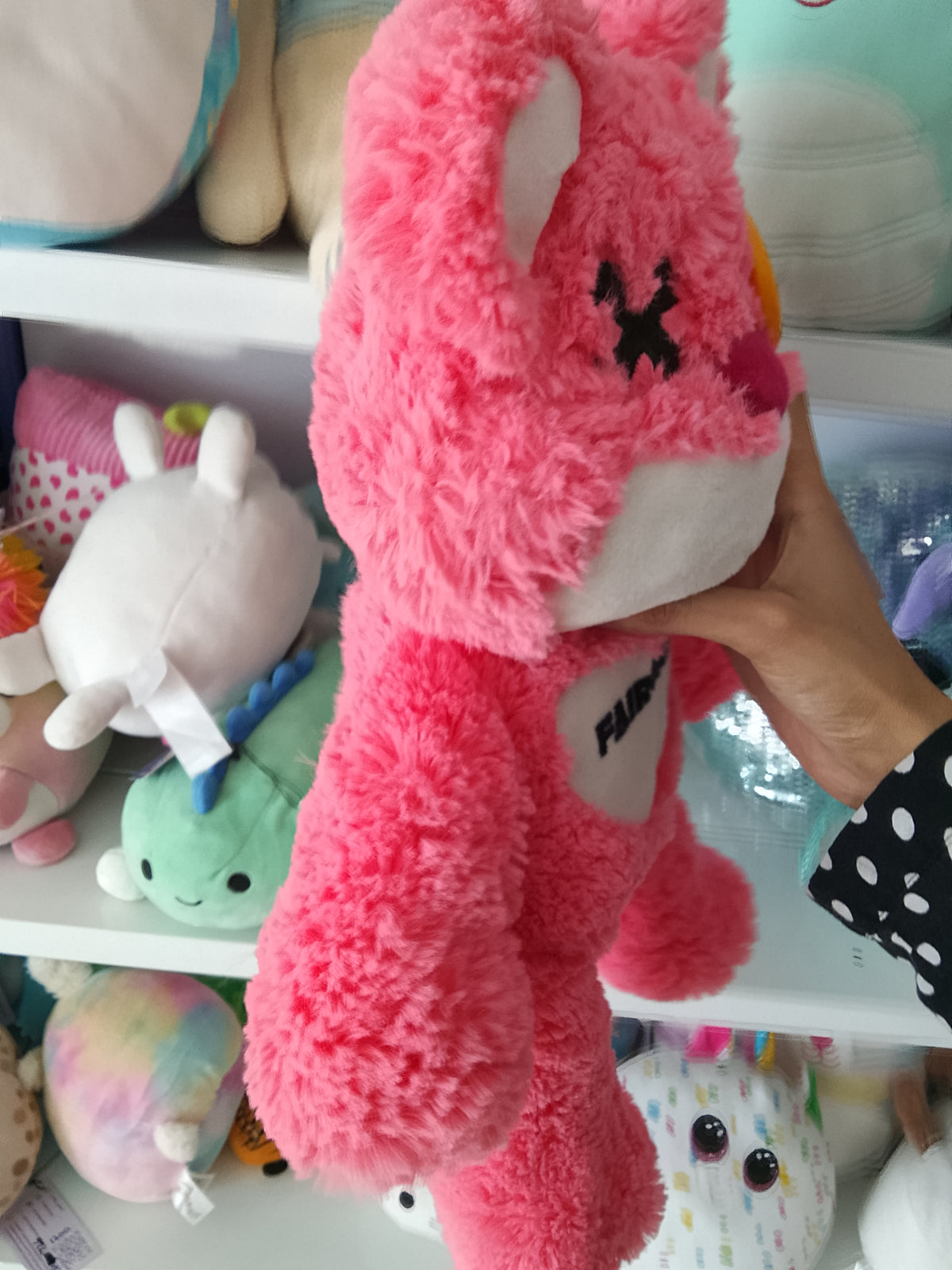 Fairgame brand pink teddy bear plush toy with a yellow button eye and a stitched "X" eye.