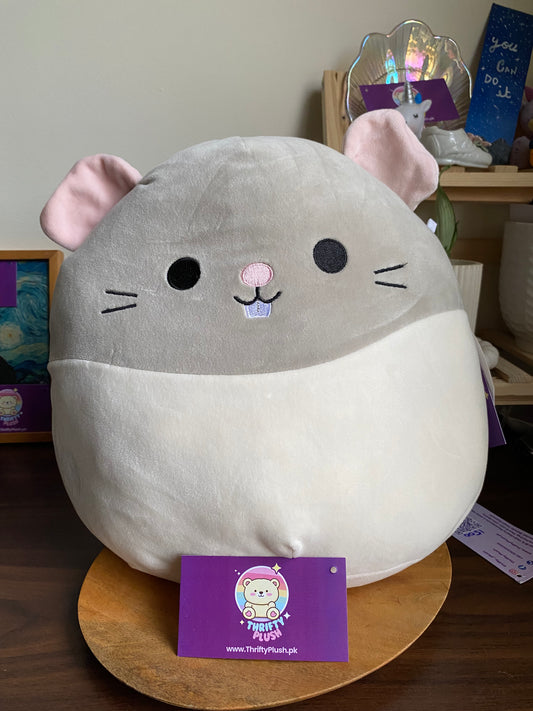 large, round, grey and white Squishmallows plush toy named Rusty, designed to resemble a rat or mouse, sitting on a wooden surface