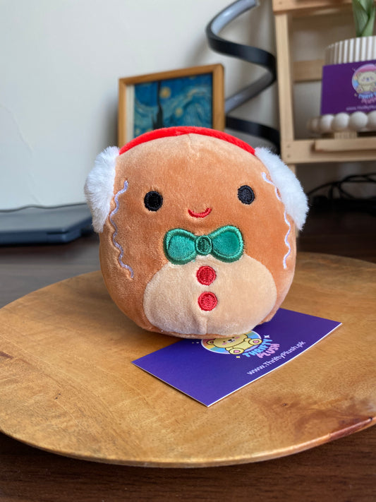 Photo of a 4-inch Squishmallows ornament plush of Jordan the Gingerbread—gingerbread-man shaped with embroidered smiling face, green bow tie, red buttons, and a red hanging loop.