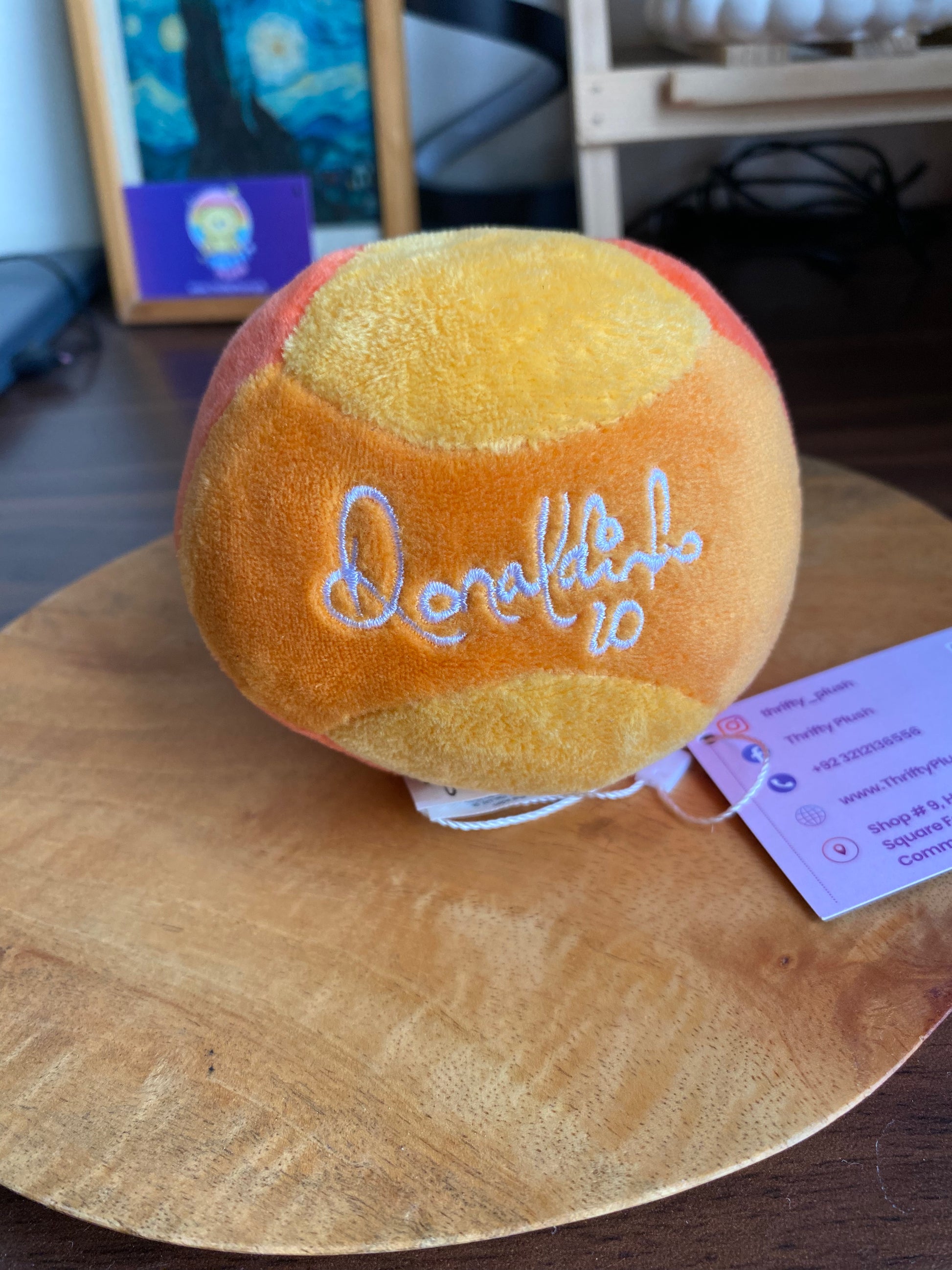 Round Donokubo plush ball in orange and yellow patchwork with white embroidered logo, displayed on a wooden surface with tags attached.