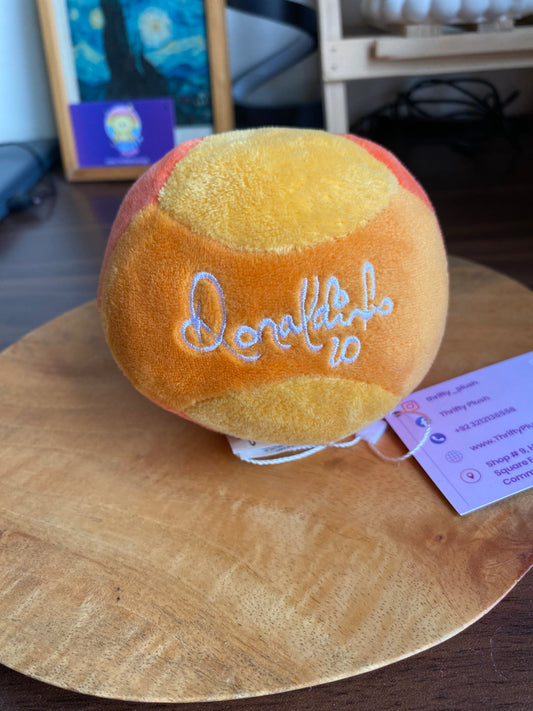 Round Donokubo plush ball in orange and yellow patchwork with white embroidered logo, displayed on a wooden surface with tags attached.