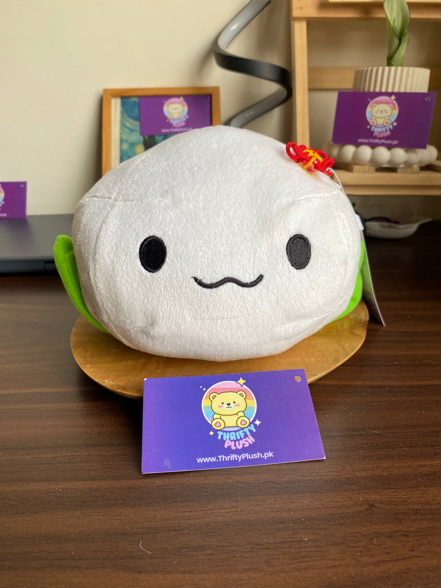 Front view of white mochi plush with cute embroidered face, green leaves, and red knot bow.