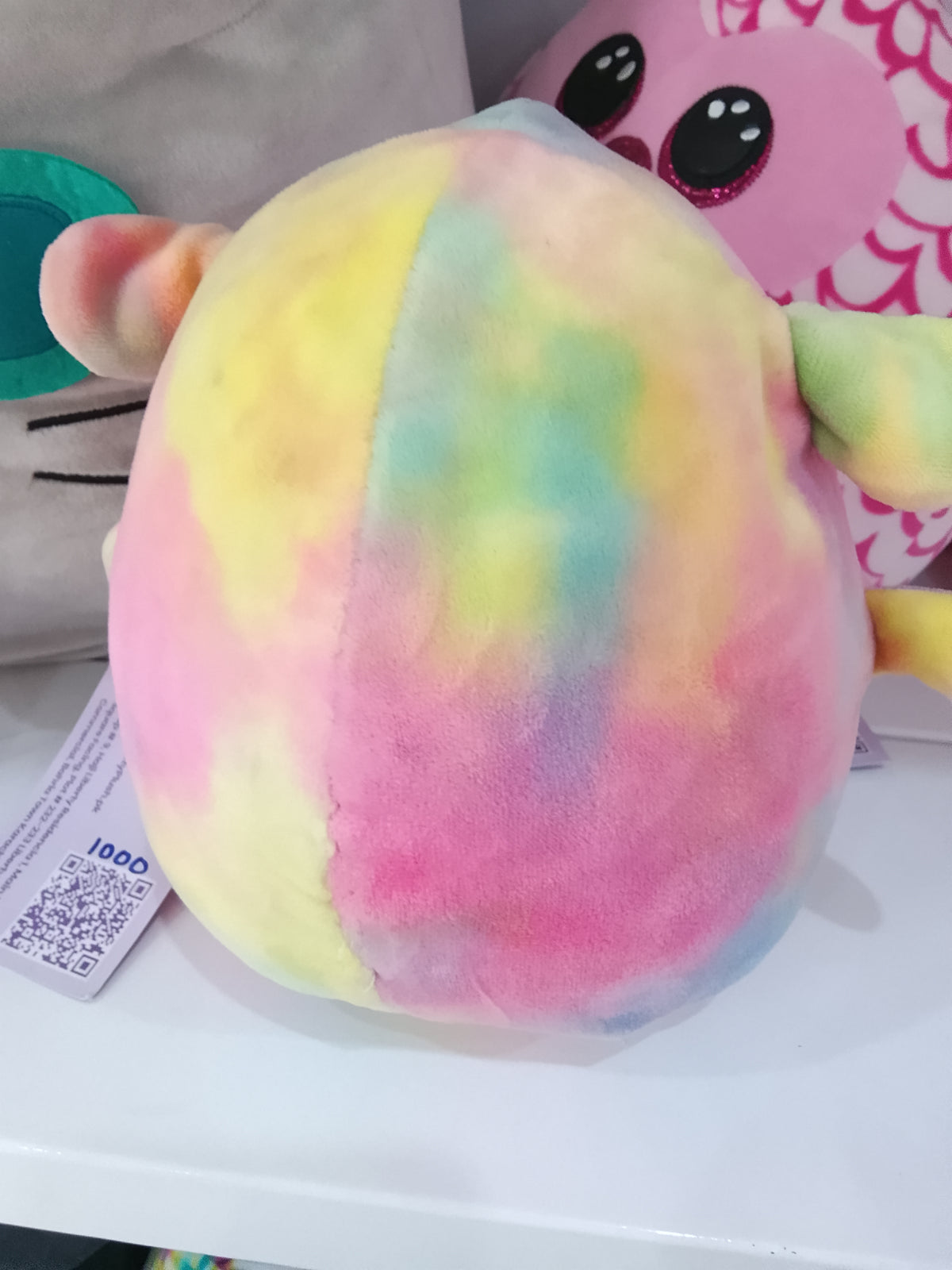 Squishmallows Lana the rainbow lamb plushie, featuring a colorful tie-dye design with embroidered flowers.