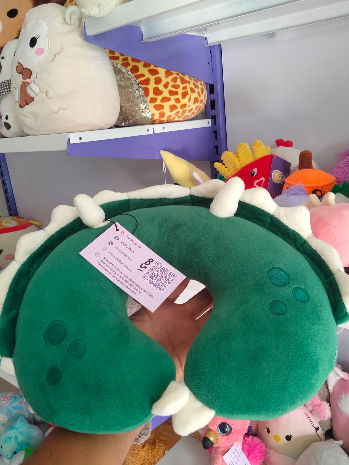 This is a green dinosaur-themed travel neck pillow from Thrifty Plush.