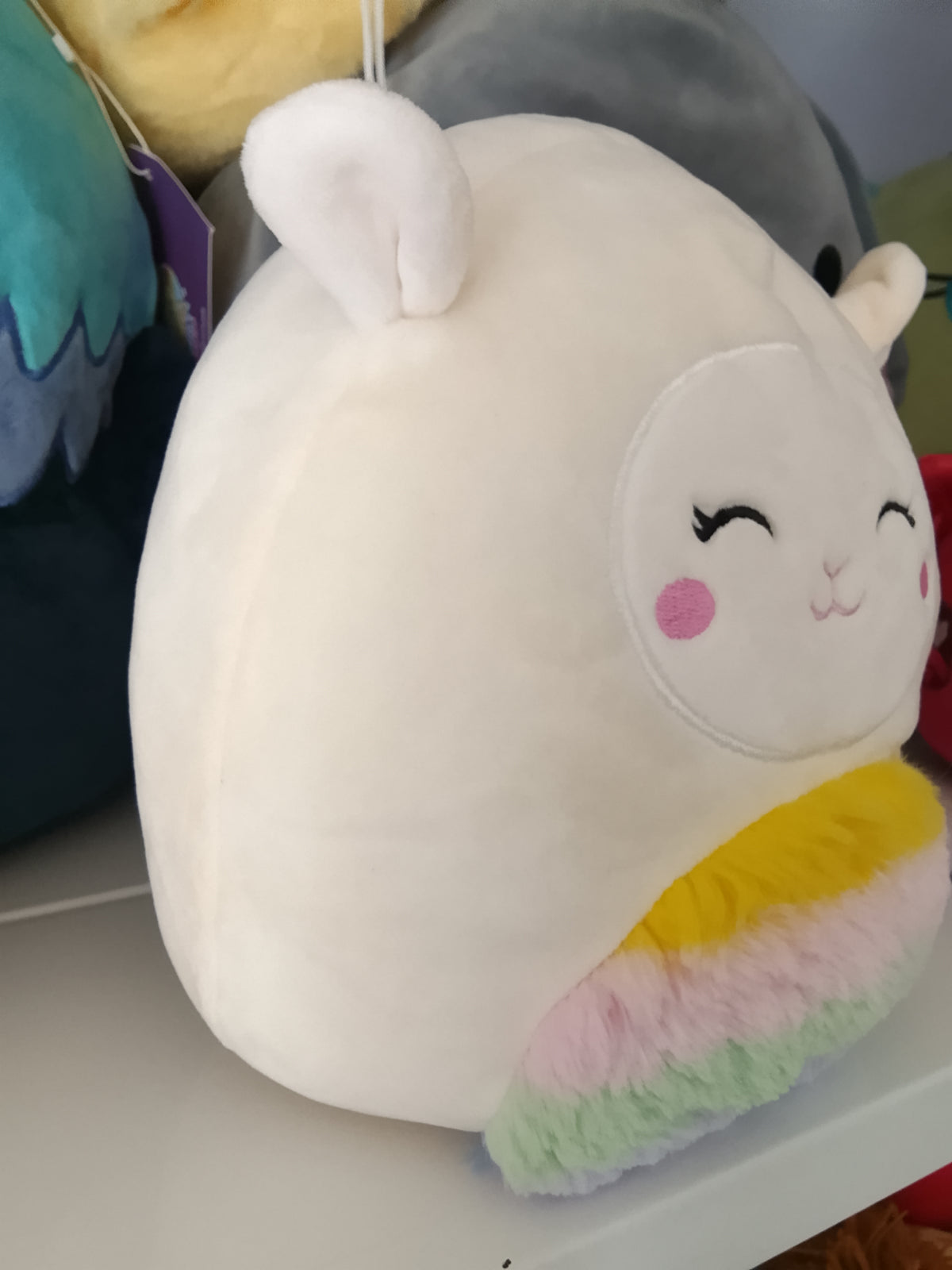 Squishmallows character Sophie the Lamb, rainbow-colored belly plush toy.
