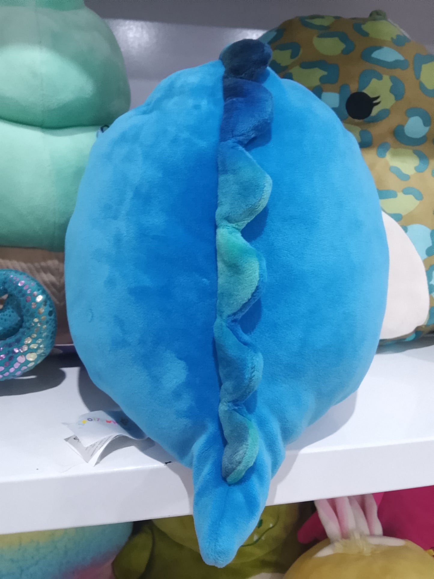 Squishmallows Brody, a blue winking dinosaur with a fuzzy white belly plush toy
