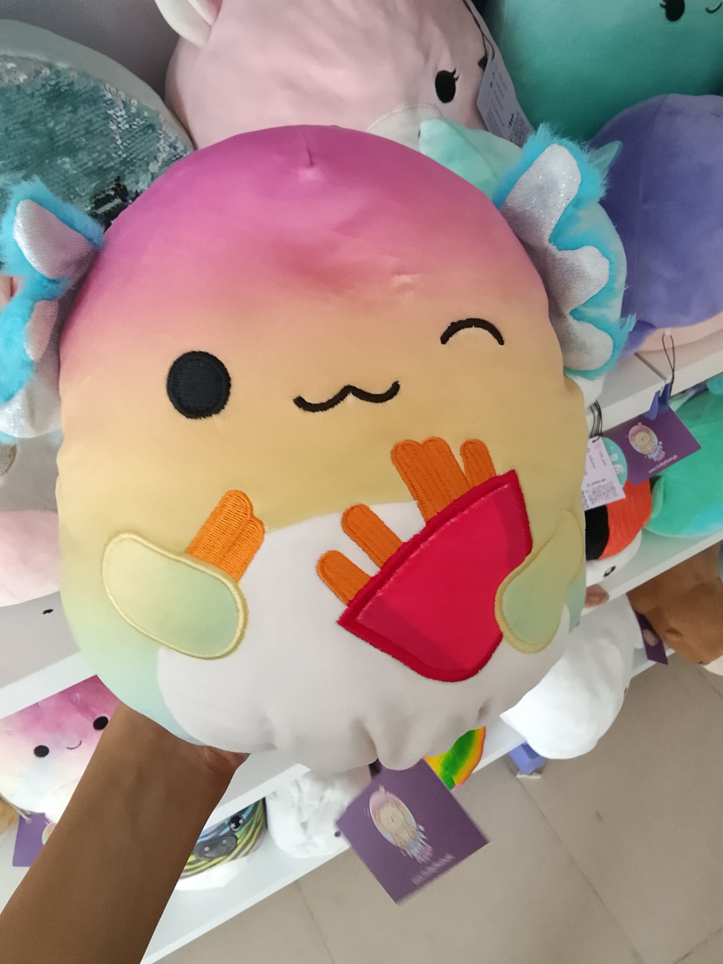 Squishmallows Flip-A-Mallows Aika the Axolotl plush rainbow design and holding a French fry carton.