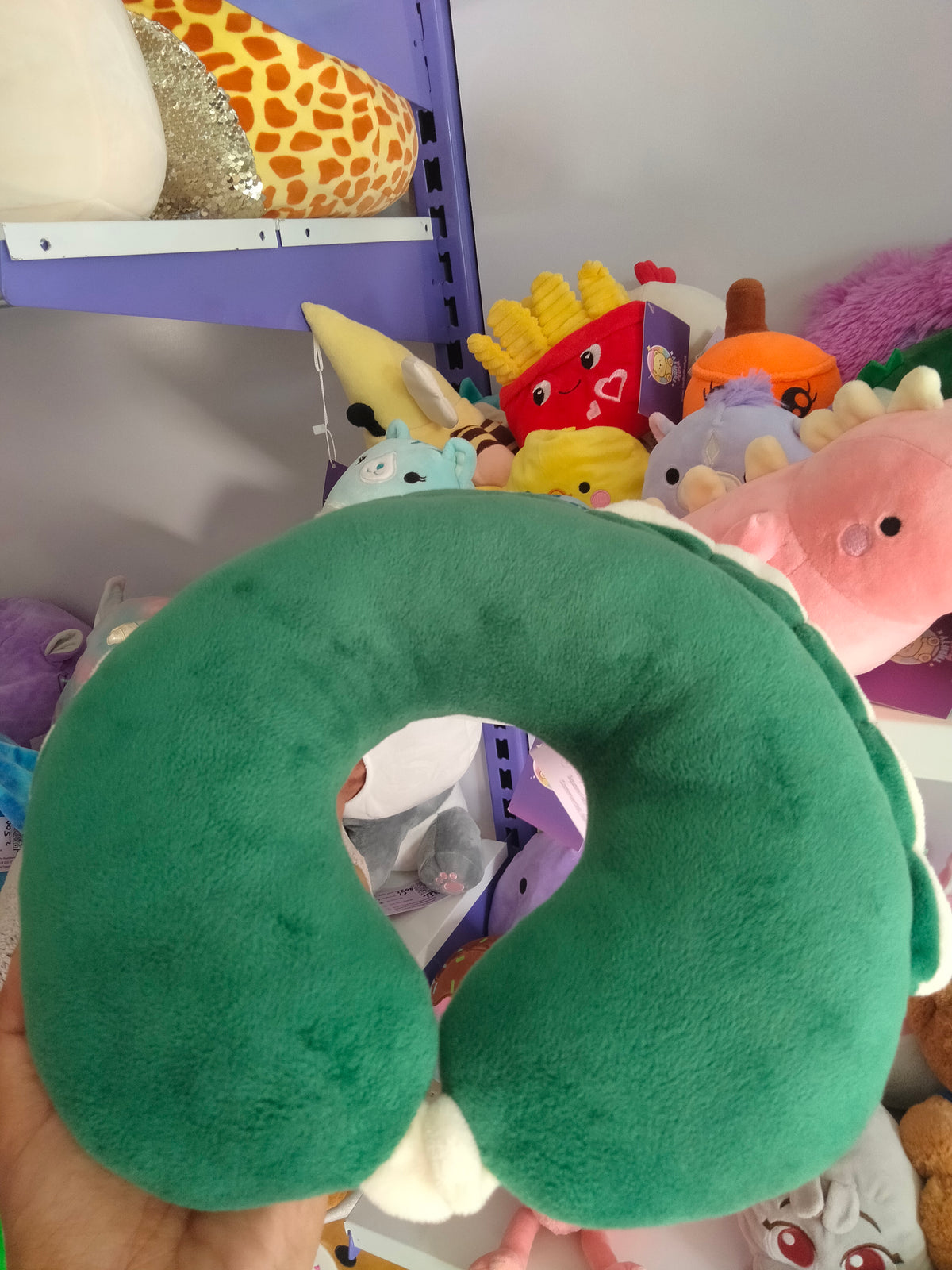 This is a green dinosaur-themed travel neck pillow from Thrifty Plush.