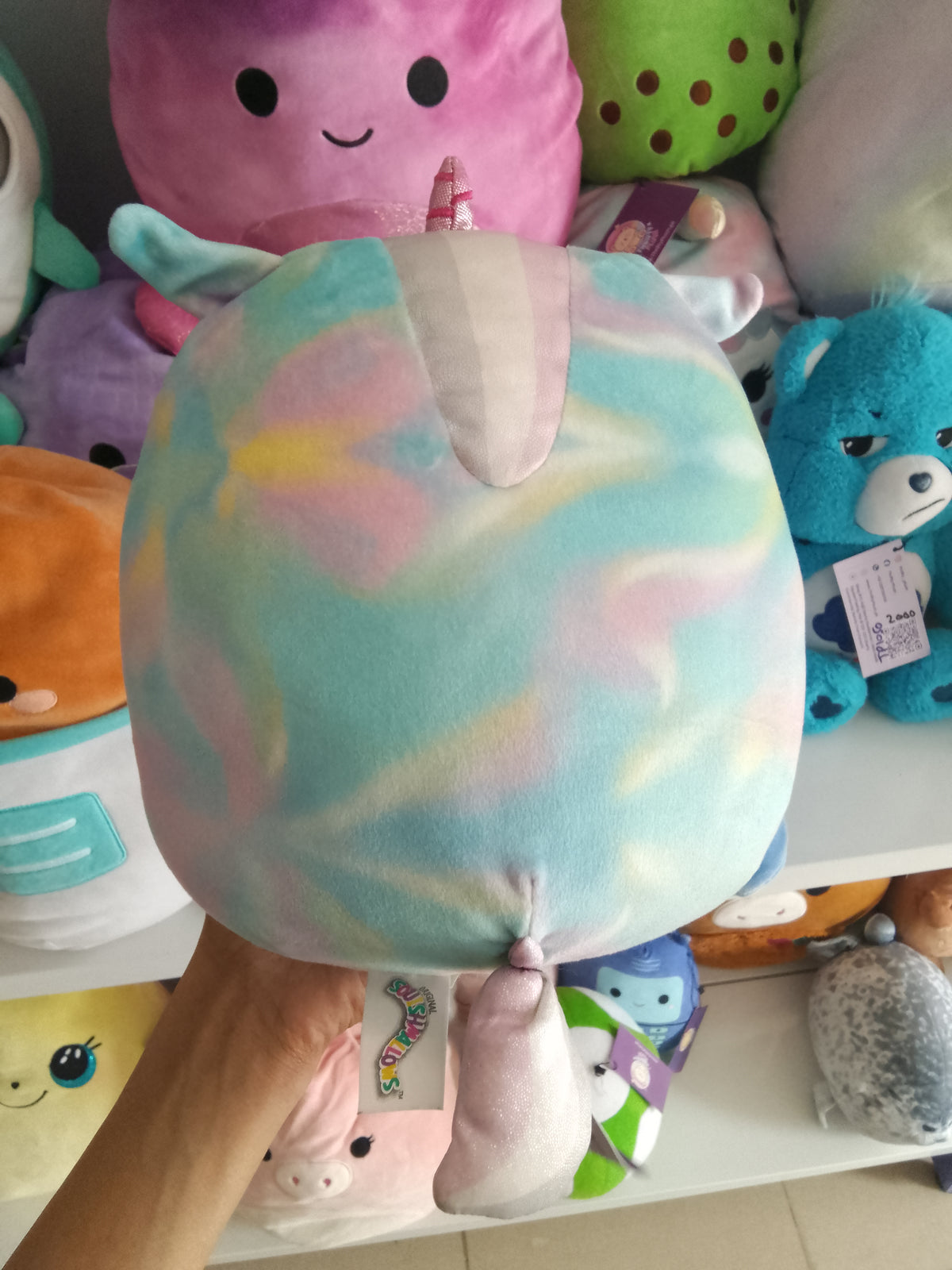 Squishmallows Kellytoys unicorn plush, possibly Rodina or Anouk Mystery Squad series, rainbow tie-dye pattern and a fluffy white belly.