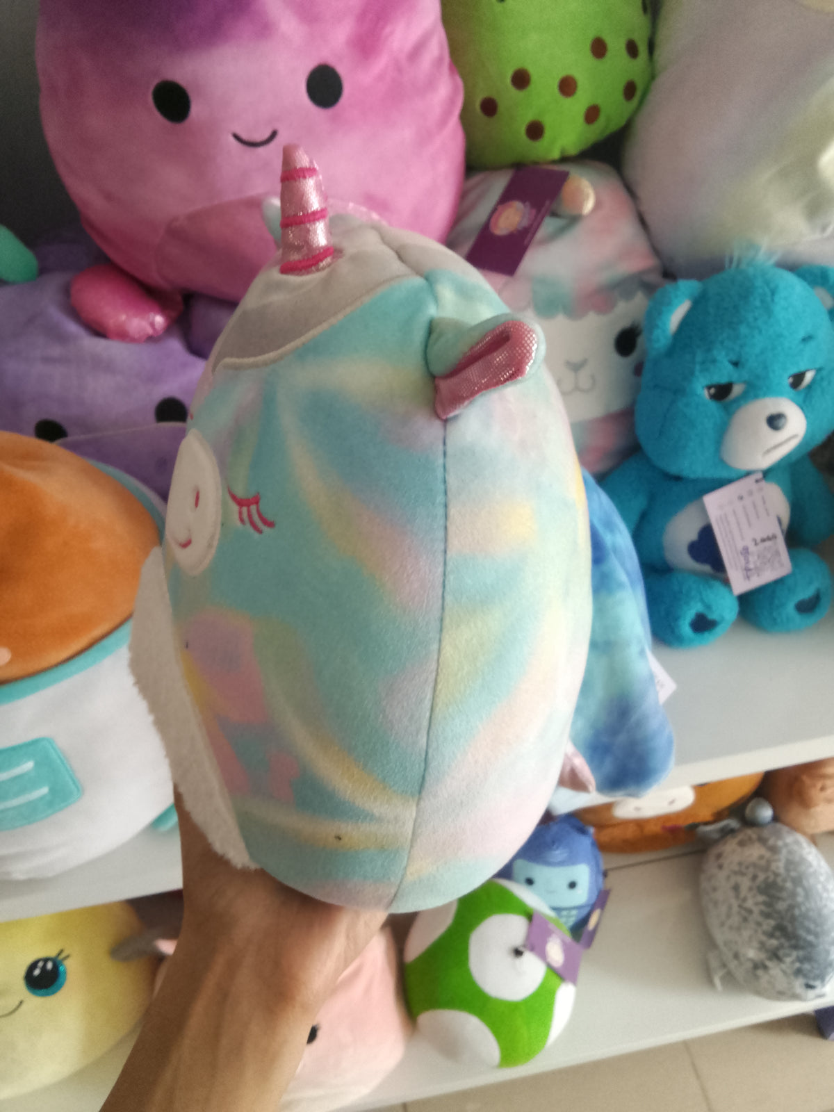 Squishmallows Kellytoys unicorn plush, possibly Rodina or Anouk Mystery Squad series, rainbow tie-dye pattern and a fluffy white belly.