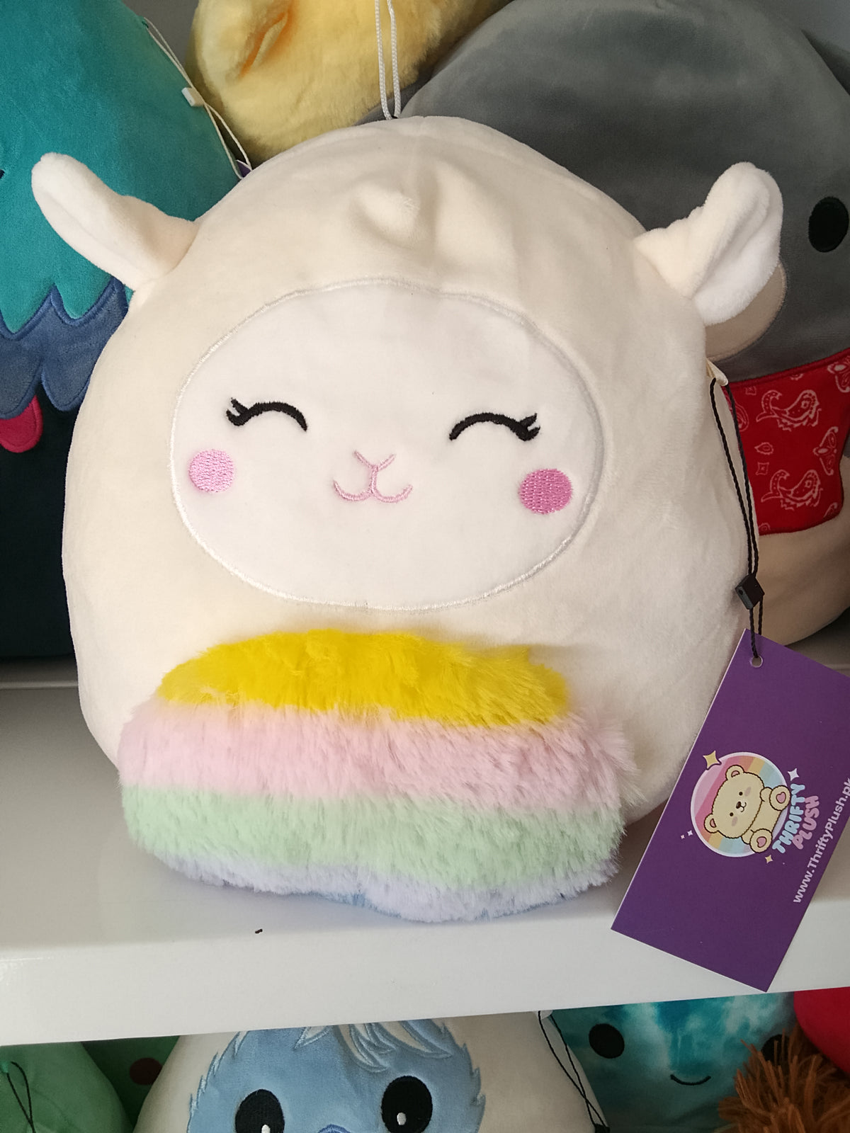 Squishmallows character Sophie the Lamb, rainbow-colored belly plush toy.