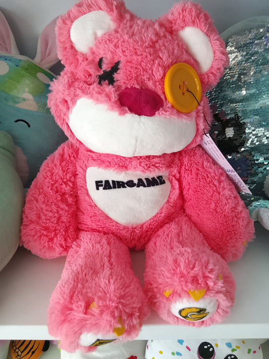 Fairgame brand pink teddy bear plush toy with a yellow button eye and a stitched "X" eye.