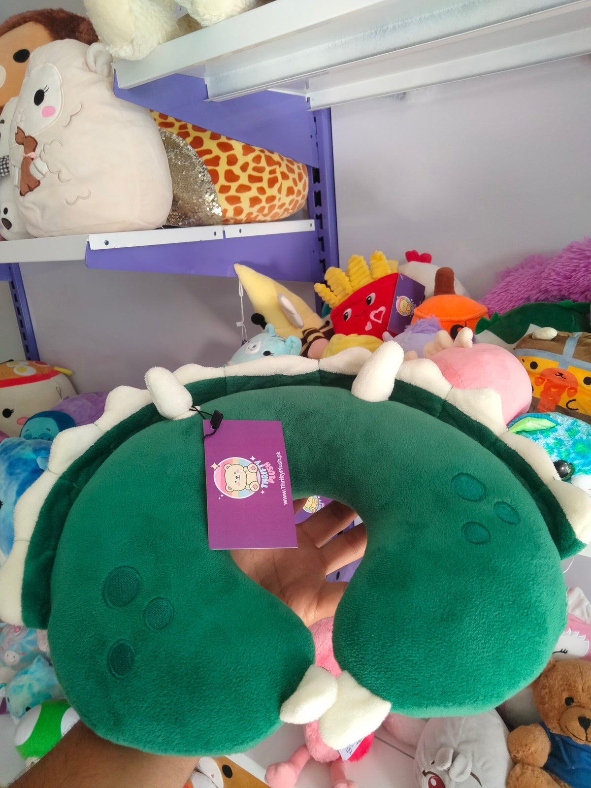 This is a green dinosaur-themed travel neck pillow from Thrifty Plush.