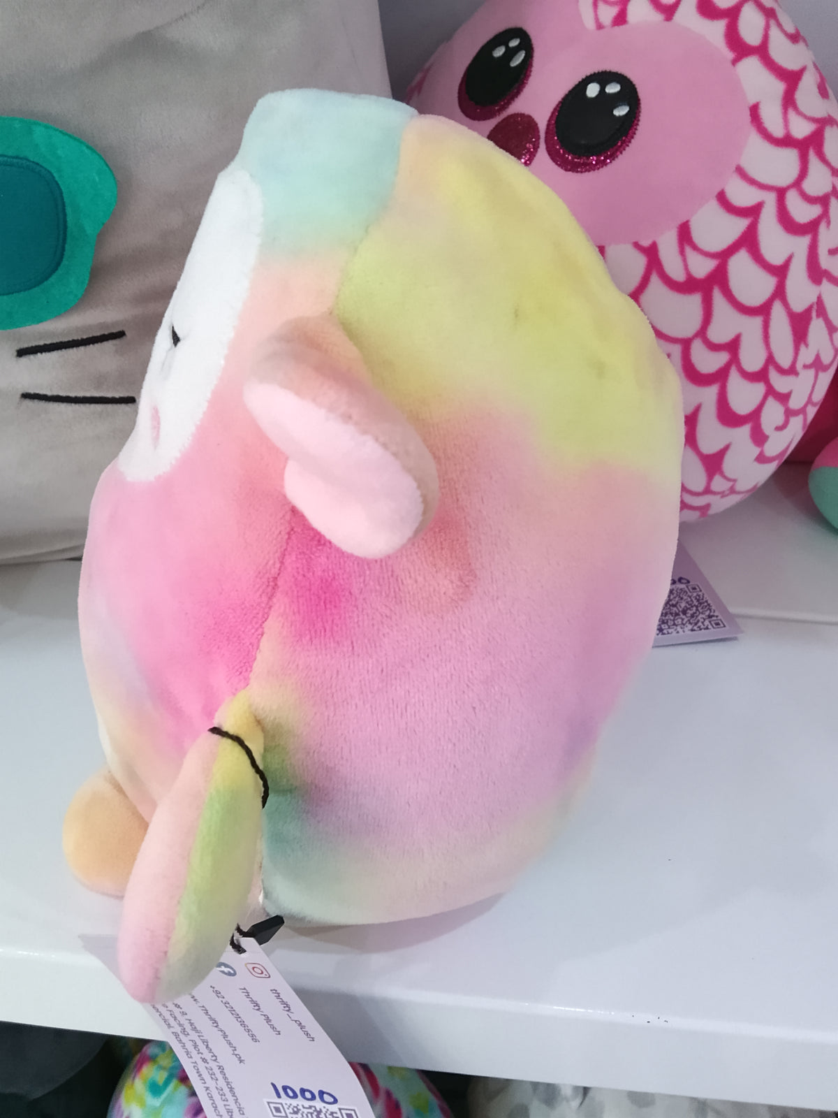 Squishmallows Lana the rainbow lamb plushie, featuring a colorful tie-dye design with embroidered flowers.